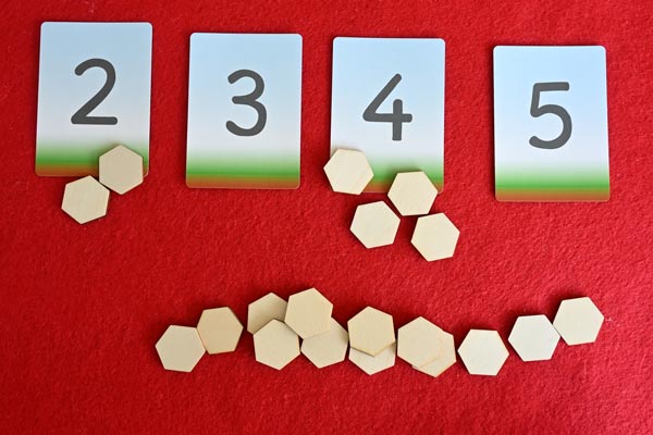 Number cards 2,3,4,and 5 on a table with various groupings of small tiles