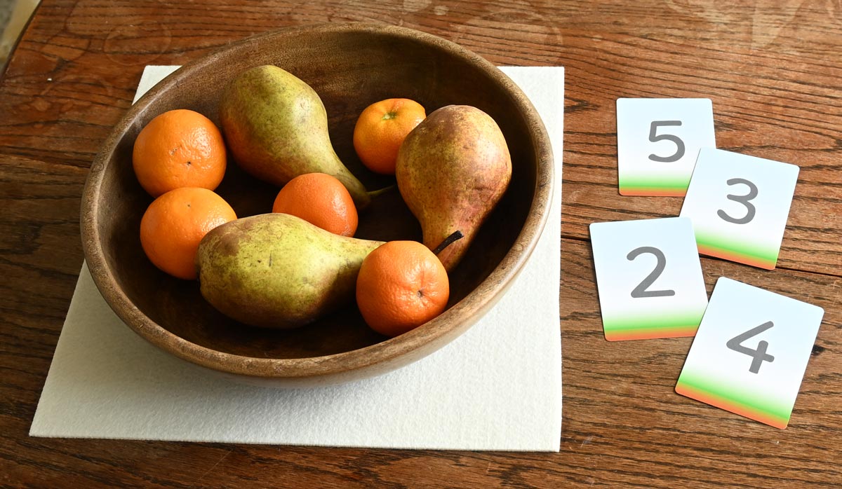 Three pears and five small oranges (mandarins) are in a bowl. Alongside are four cards showing the digits '2','3', '4','5'